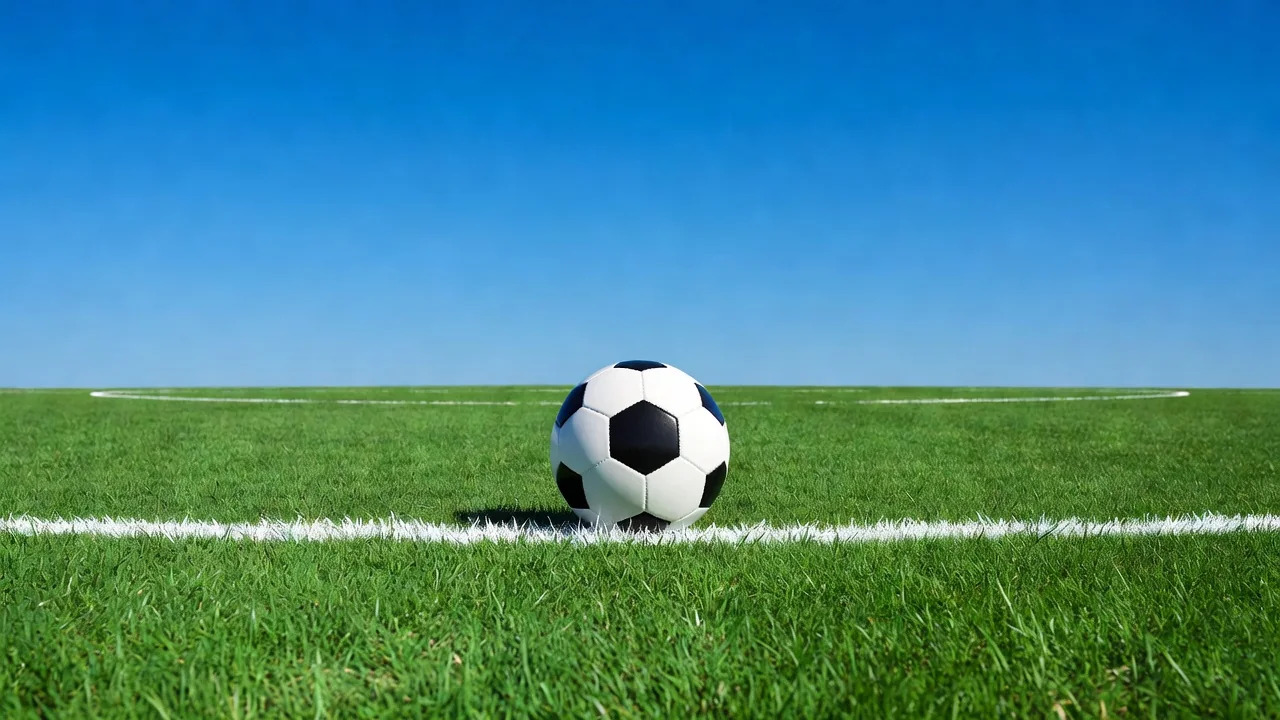 Bola de futebol sobre a linha branca do gol com o céu azul do mar ao fundo