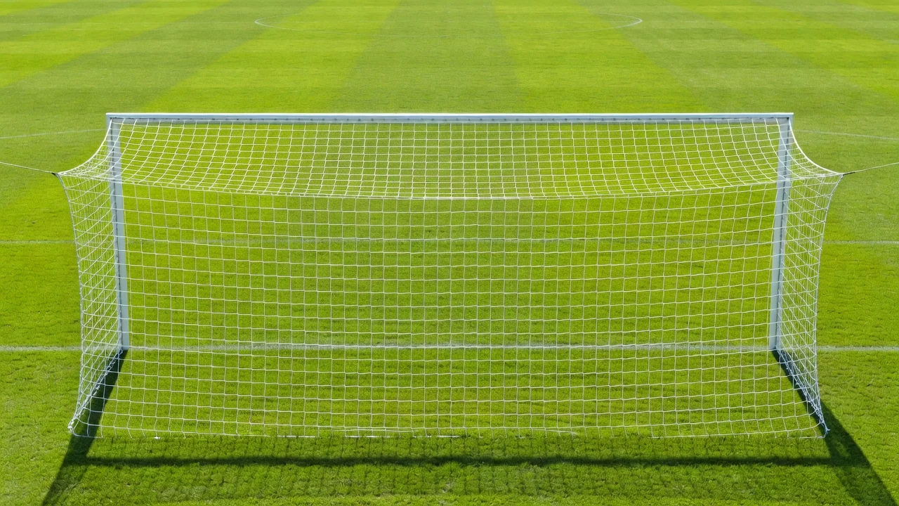 Rede de gol vista por trás em dia ensolarado, com o gramado verde ao fundo