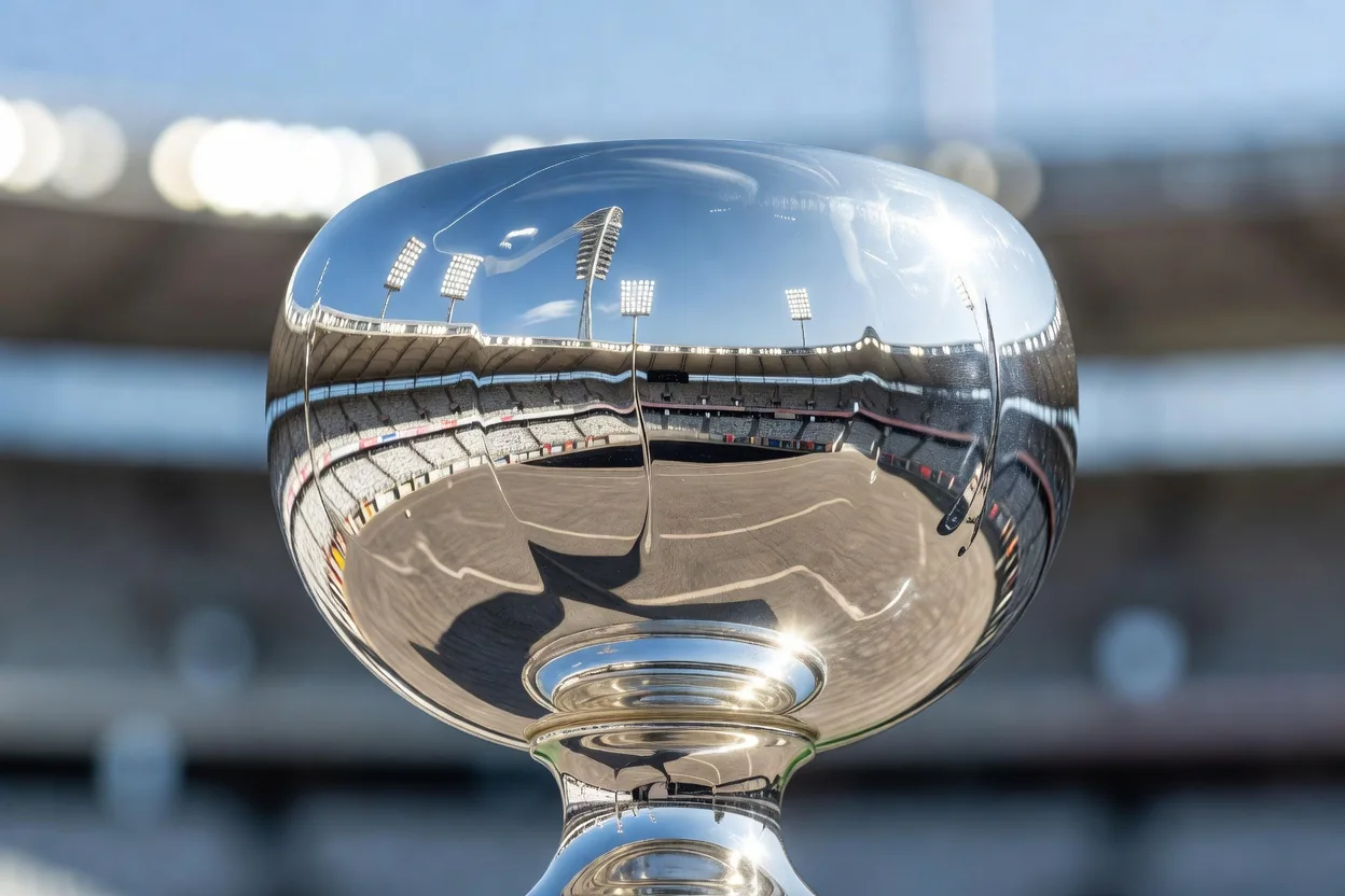 Detalhe de taça de prata refletindo as luzes de um estádio, sem inscrições