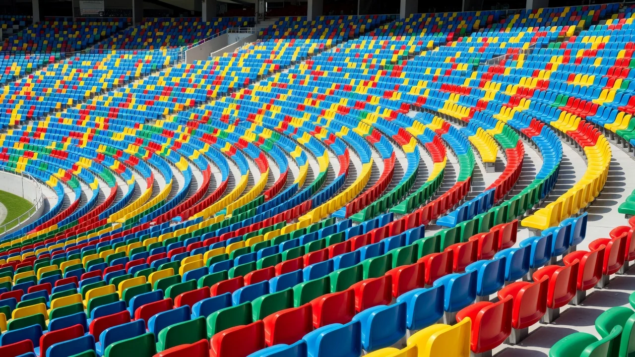 Fileiras curvas de assentos coloridos de um grande estádio sob luz clara, vazios